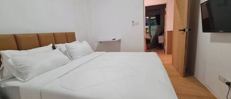 A bedroom with a bed, a nightstand, a TV, and a door leading to another room.