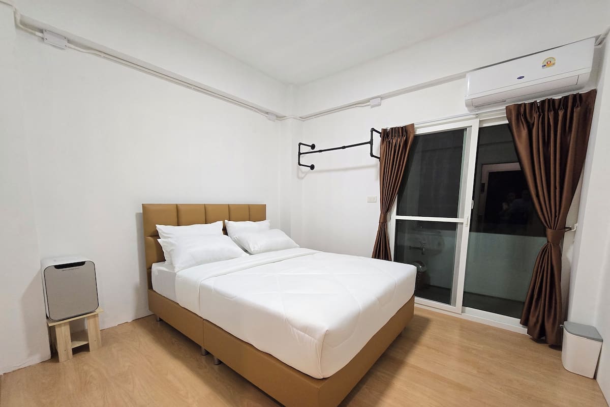 Una habitación de hotel moderna con cama, una mesita de noche, una ventana con cortinas y un equipo de aire acondicionado.