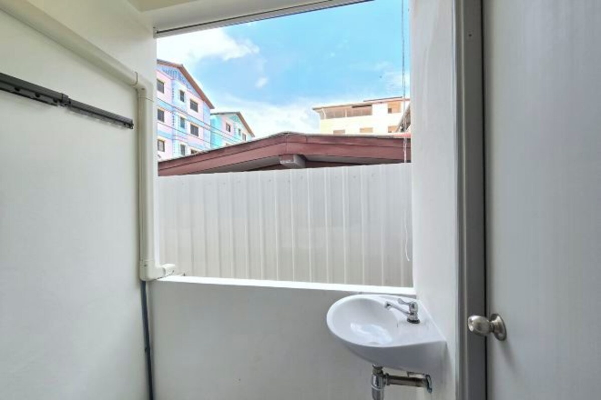 Ein kleines Badezimmer mit einem weißen Waschbecken, einem Fenster und Blick auf farbenfrohe Gebäude.