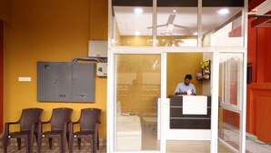 A reception area with a receptionist desk, a glass door leading to a room, and a ceiling fan. - Sree Sri Residency ECR (Chennai)