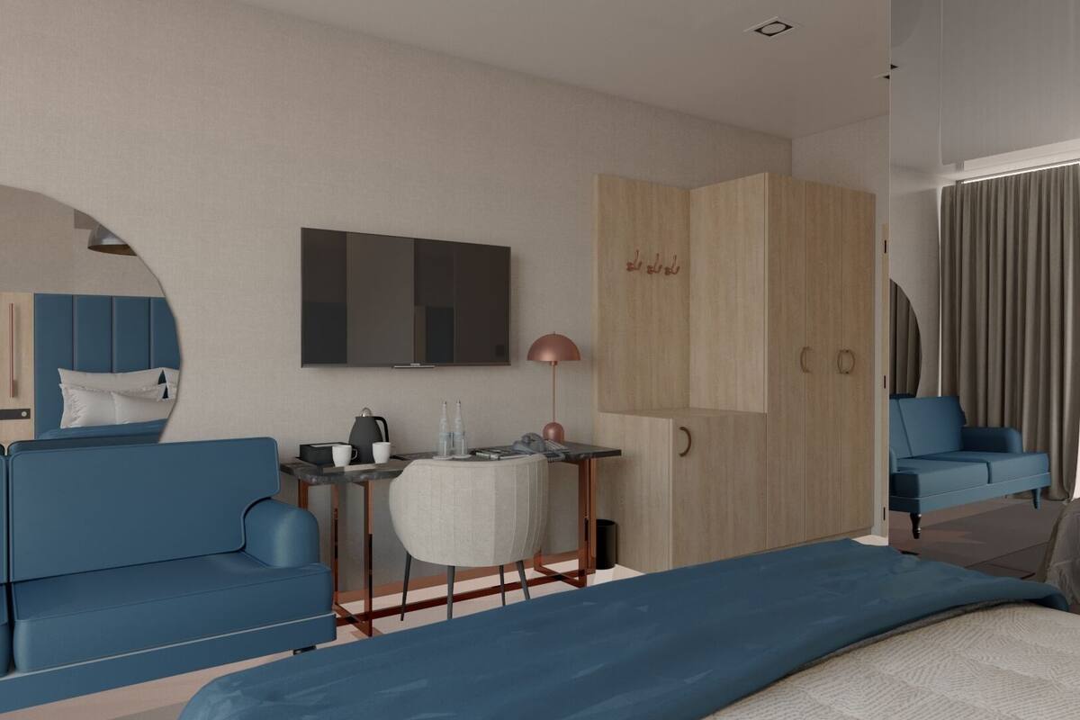 Een moderne hotelkamer met een blauwe bank, een bed, een bureau met een lamp, een televisie en een kledingkast.
