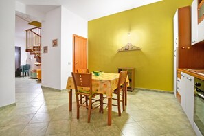 A dining area with a table and chairs, a kitchen with cabinets, and a staircase leading to another room. - Casa Plaja (Scicli)