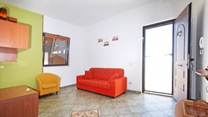 A living room with a red sofa, a yellow armchair, and a wooden cabinet. - Casa Plaja (Scicli)