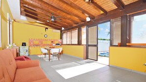 A bright room with a wooden ceiling, a yellow wall, a dining area with a table and chairs, and a sliding glass door leading to a pool. - Casa Plaja (Scicli)