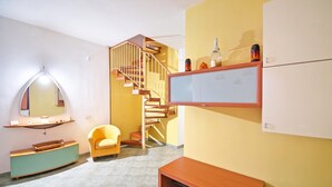 A room with a wooden staircase, a yellow wall, a wooden bench, a chair, and a flat-screen TV mounted on the wall. - Casa Plaja (Scicli)