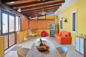 Une pièce avec un plafond en bois, un canapé rouge, une table avec des fruits et un fauteuil en forme de sac de haricots rouge.