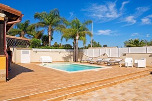 Una piscina con sillas de descanso y palmeras al fondo.
