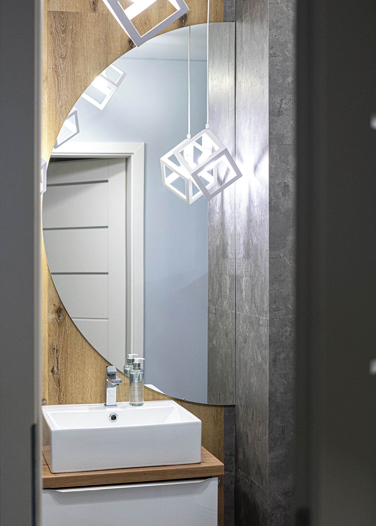 Un baño con lavamanos blanco, encimera de madera y un espejo grande con lámpara de diseño geométrico.