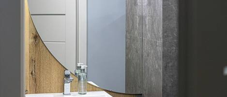 Un baño con lavamanos blanco, encimera de madera y un espejo grande con lámpara de diseño geométrico.