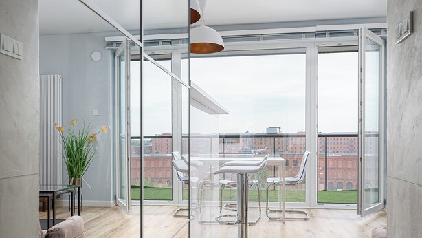 Zona pranzo moderna con parete divisoria in vetro, soffitto bianco e vista su un edificio sullo sfondo.