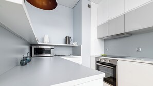 Una cucina moderna con mobili bianchi, un forno a microonde integrato, un forno e un bollitore in acciaio inossidabile sul piano di lavoro.