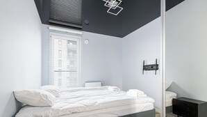 Una camera da letto moderna con un letto, un comodino, una base di ricarica a parete e una finestra con persiane.