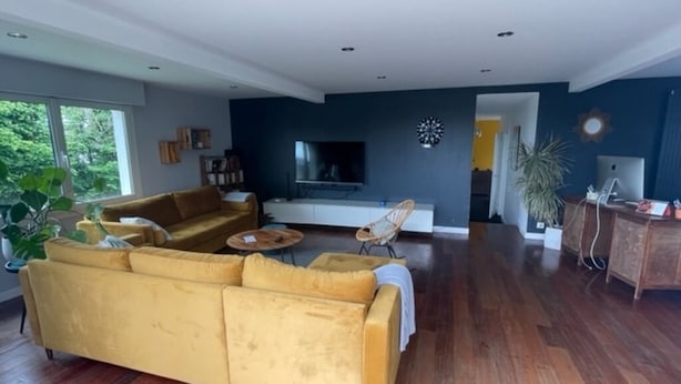 Una sala de estar moderna con un sofá amarillo, suelo de madera, un televisor de pantalla plana y un comedor con mesa y sillas.