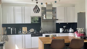 Una cocina moderna con armarios blancos, una isla de madera con dos sillas, una cafetera y un hervidor.