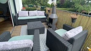 Un patio exterior con mobiliario de mimbre, una parrilla para barbacoa y una vista de una casa al fondo.