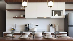 A modern kitchen with white cabinets, a microwave, a coffee maker, and a dining table set with bowls and glasses.