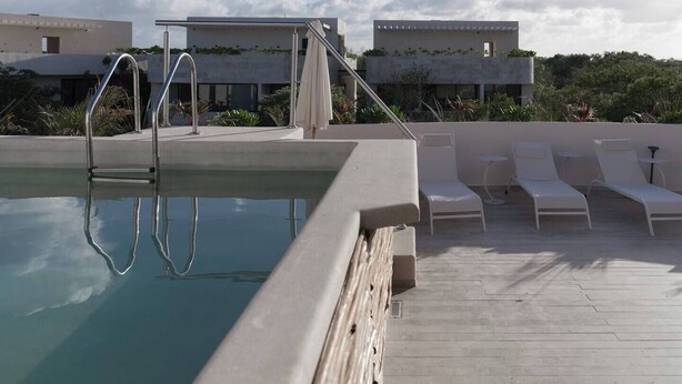 A rooftop pool with a clear view of the sky, a few lounge chairs, and a modern building in the background.