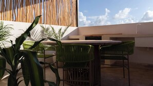 An outdoor patio with a round table and green chairs, a bamboo wall, and a view of the sky.