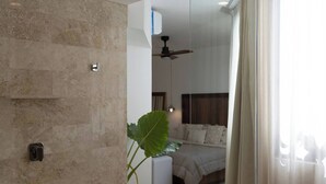 A modern bathroom with a stone wall, a shower, and a glass door leading to a bedroom.