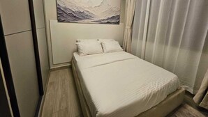 A bedroom with a bed, a painting of mountains on the wall, and a window with curtains.