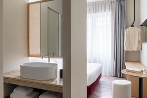 A modern bathroom with a round sink, a mirror, and a towel rack.