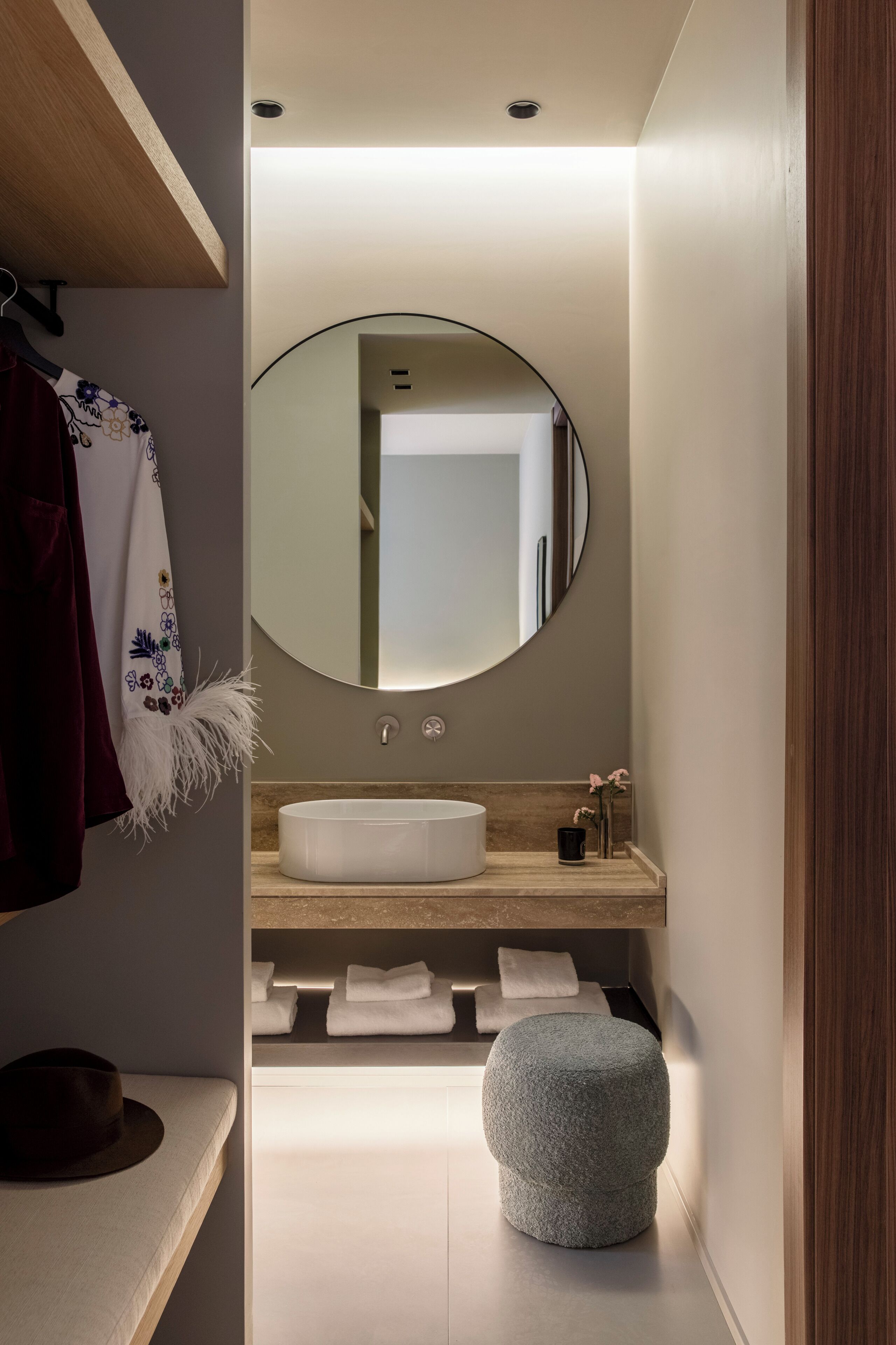 A modern bathroom with a round mirror, a white sink, and a small stool.