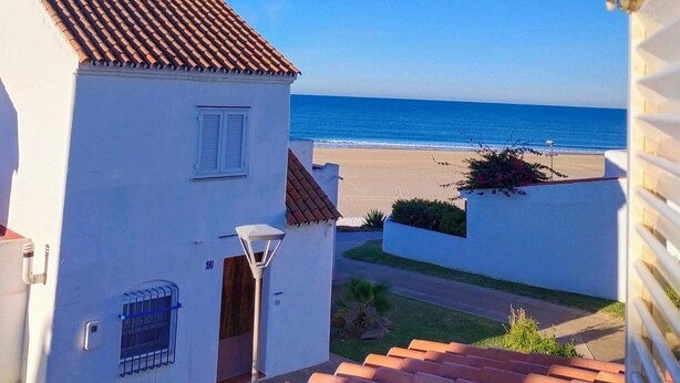 A coastal view with a white building, red-tiled roof, and a clear blue sky. - Beautiful house 30 meters from the sea (Almonte)