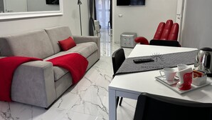 En moderne stue med en grå sofa, røde puder, et hvidt bord med bakke, et fladskærms-tv og en grå skammel.