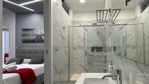 Et moderne badeværelse med en brusekabine i glas, en stor hvid vask og et spejl med marmorbagplade.