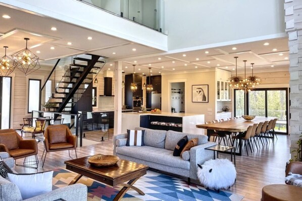 Een ruime woonkamer met een moderne bank, een eettafel en een trap naar een hoger gelegen verdieping.