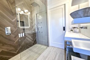 Een moderne badkamer met een douchecabine van glas, een grote spiegel en een wastafelmeubel met wastafel en aanrecht.