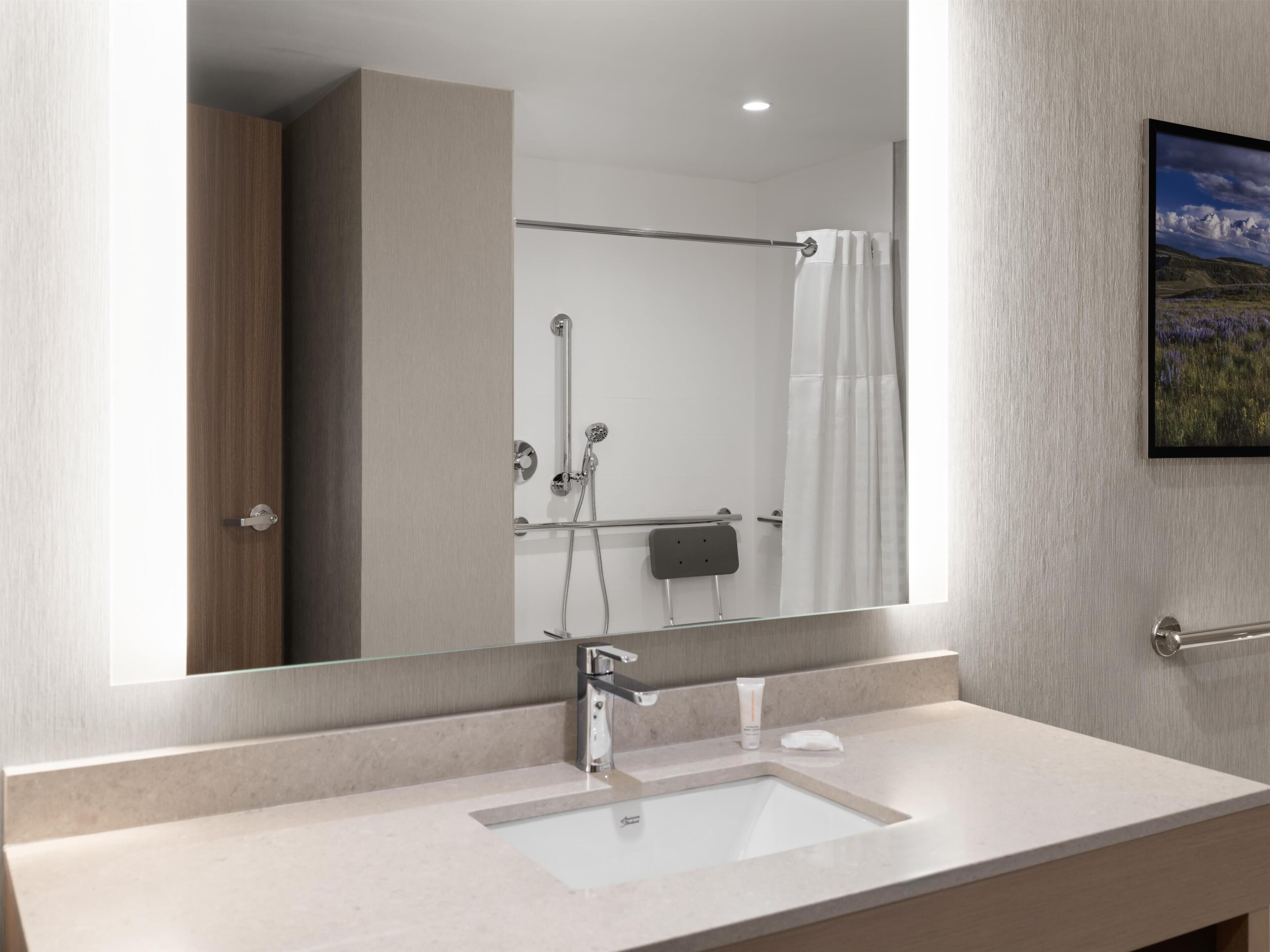 Une salle de bain moderne avec un grand miroir, un lavabo en verre, une douche avec une porte en verre et un porte-serviettes.