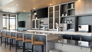 Zona de bar moderna con una barra larga, varios taburetes y una variedad de utensilios y botellas.