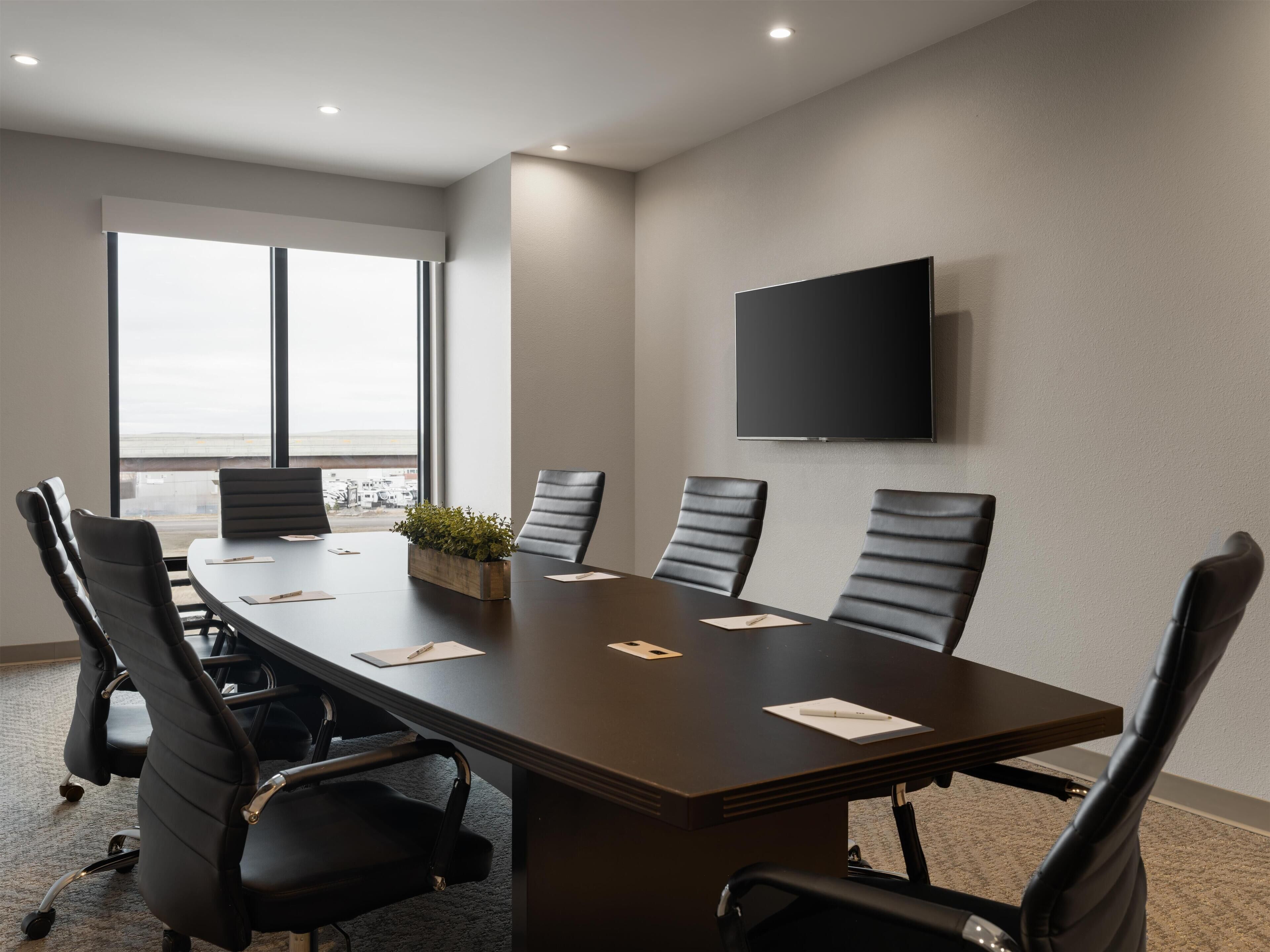 A conference room with a long table, six chairs, a flat-screen TV, and a large window with a view.