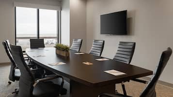 A conference room with a long table, six chairs, a flat-screen TV, and a large window with a view.