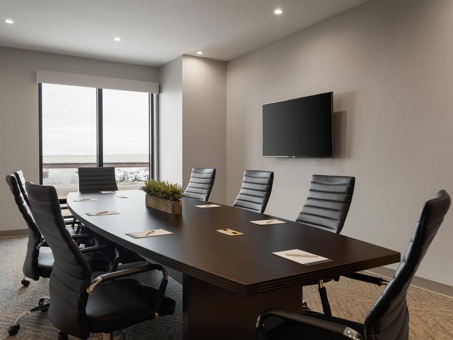 A conference room with a long table, six chairs, a flat-screen TV, and a large window with a view.
