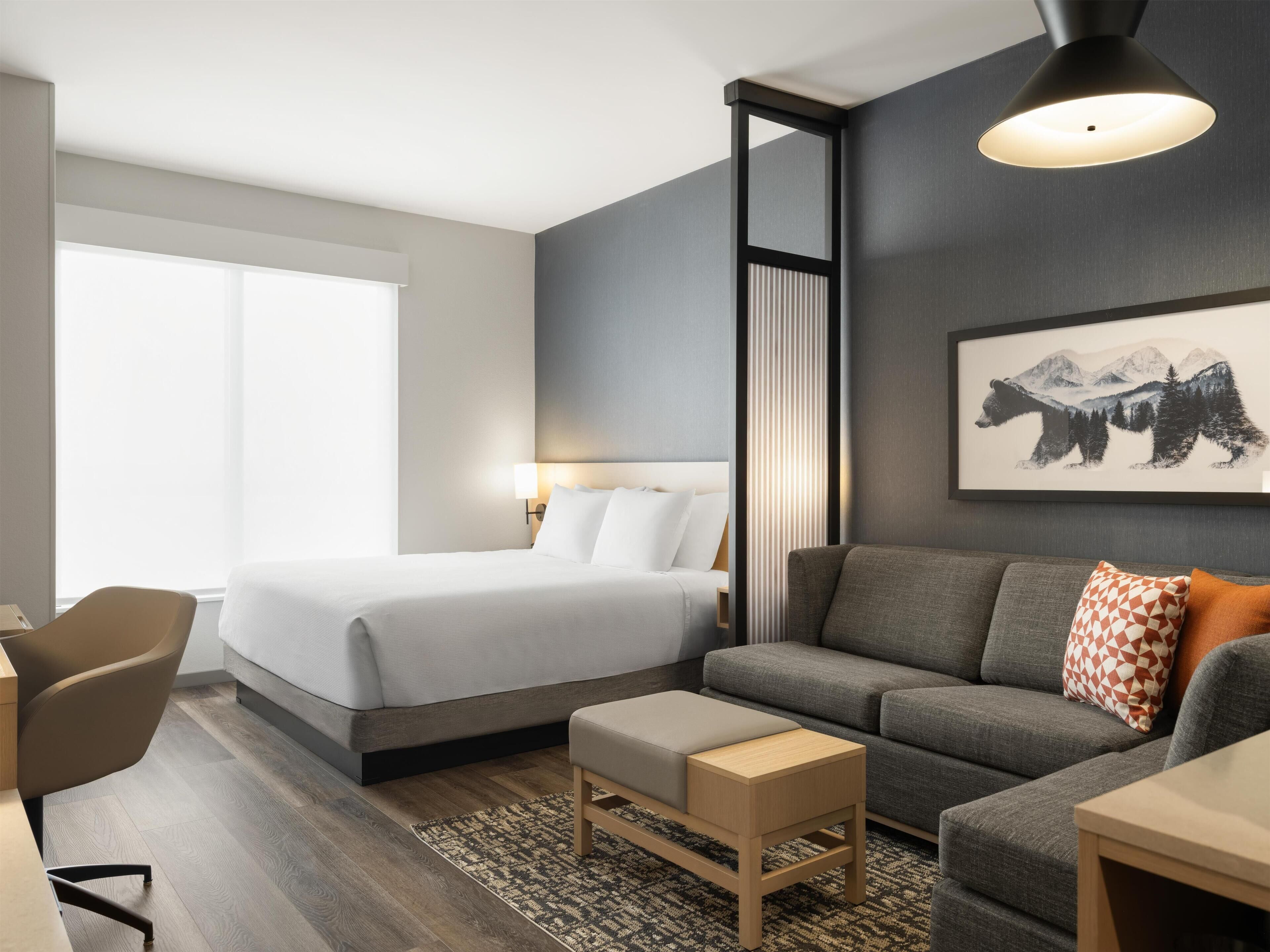 A modern hotel room with a bed, a sofa, a desk, and a chair.