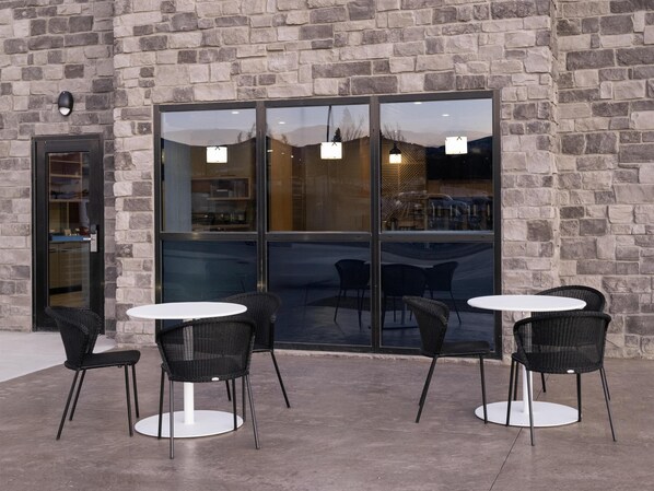 Un espace extérieur aménagé avec des murs en pierre et des portes vitrées, comprenant des tables rondes et des chaises en osier.
