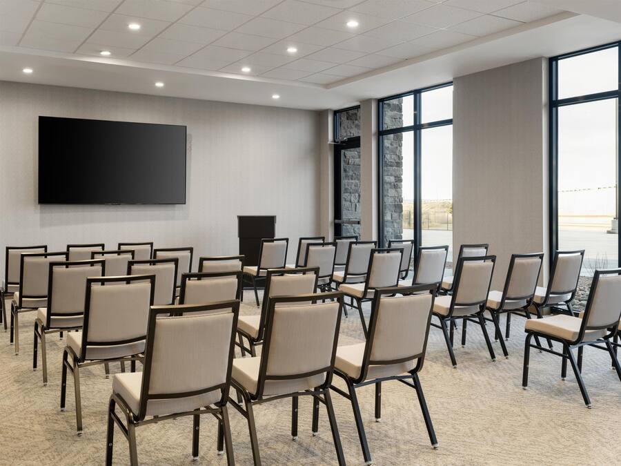Un salón de conferencias con filas de sillas, una pantalla grande y un atril.
