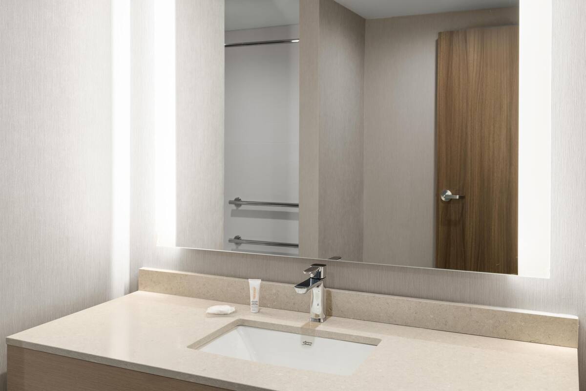 A modern bathroom with a large mirror, a sink, and a wooden door.