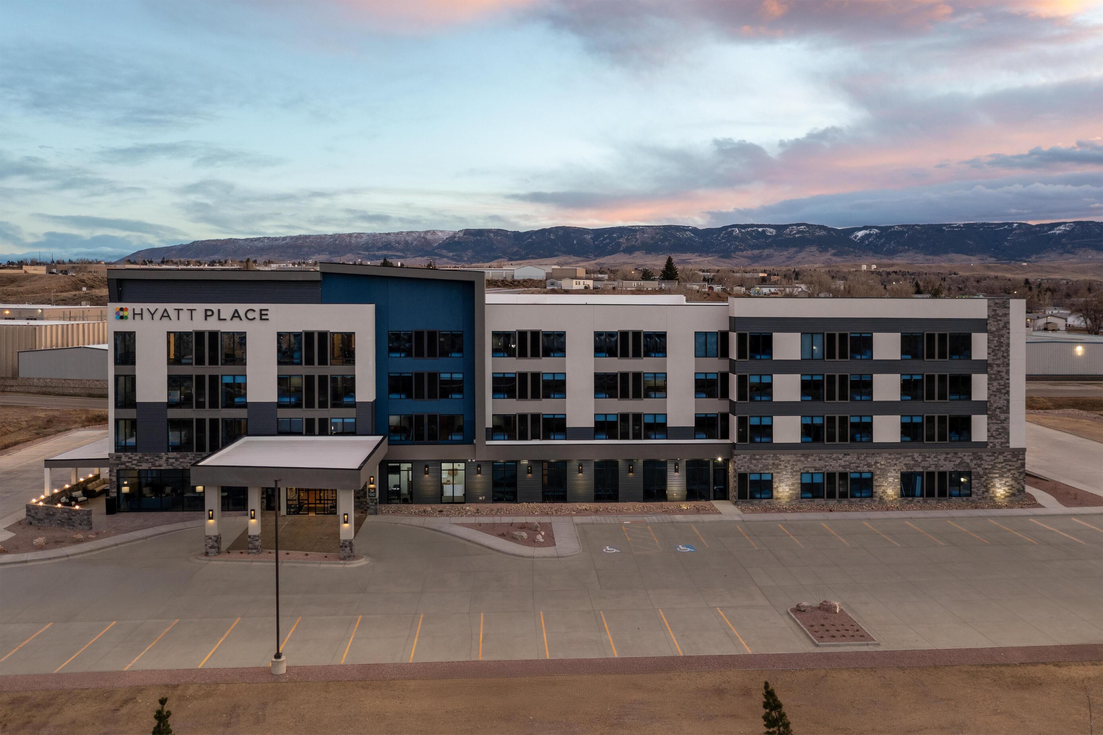 A Hyatt Place hotel with a modern design, featuring a parking lot and a view of mountains in the background.