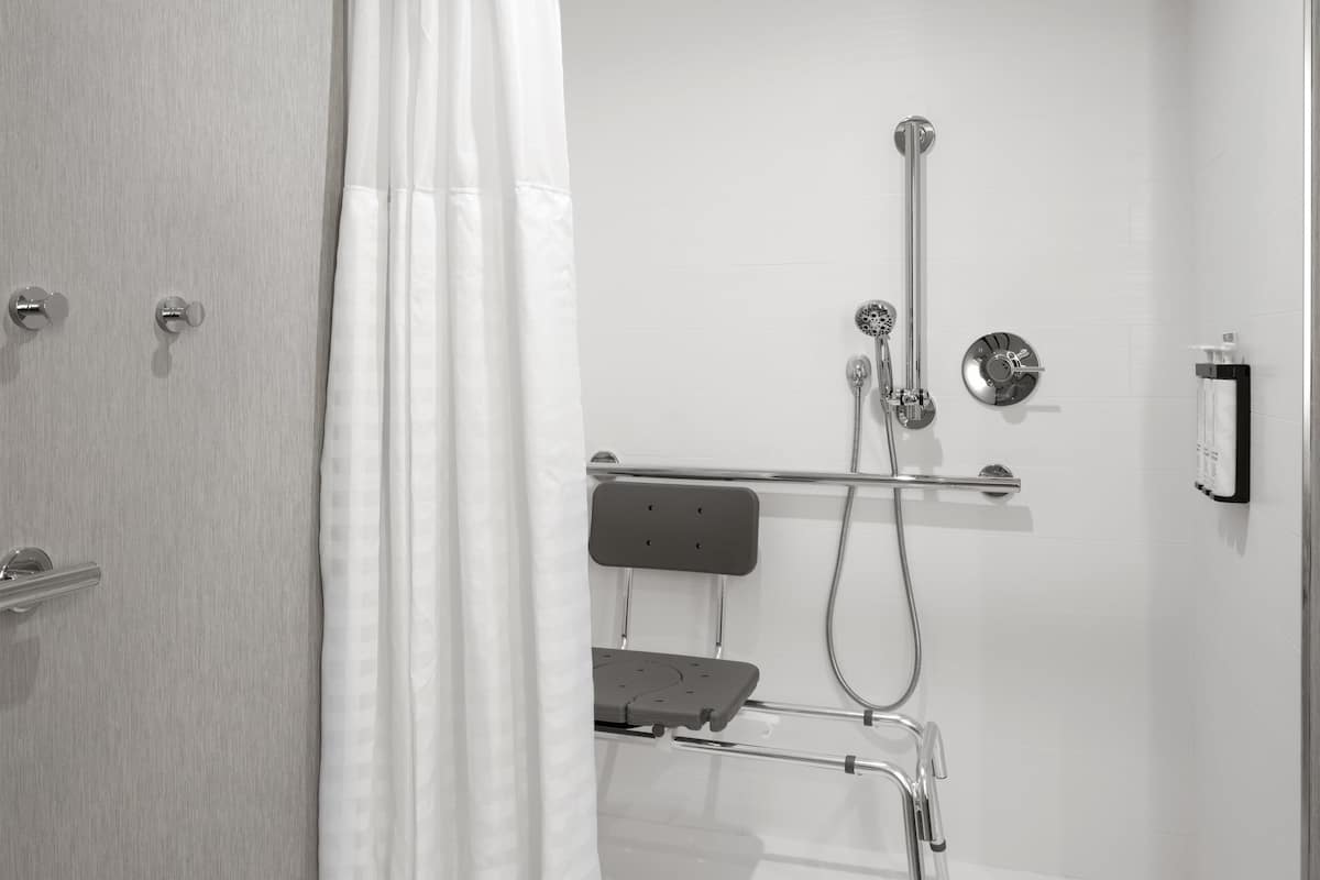A modern bathroom with a shower, a handheld showerhead, a handheld shower attachment, and a towel dispenser.