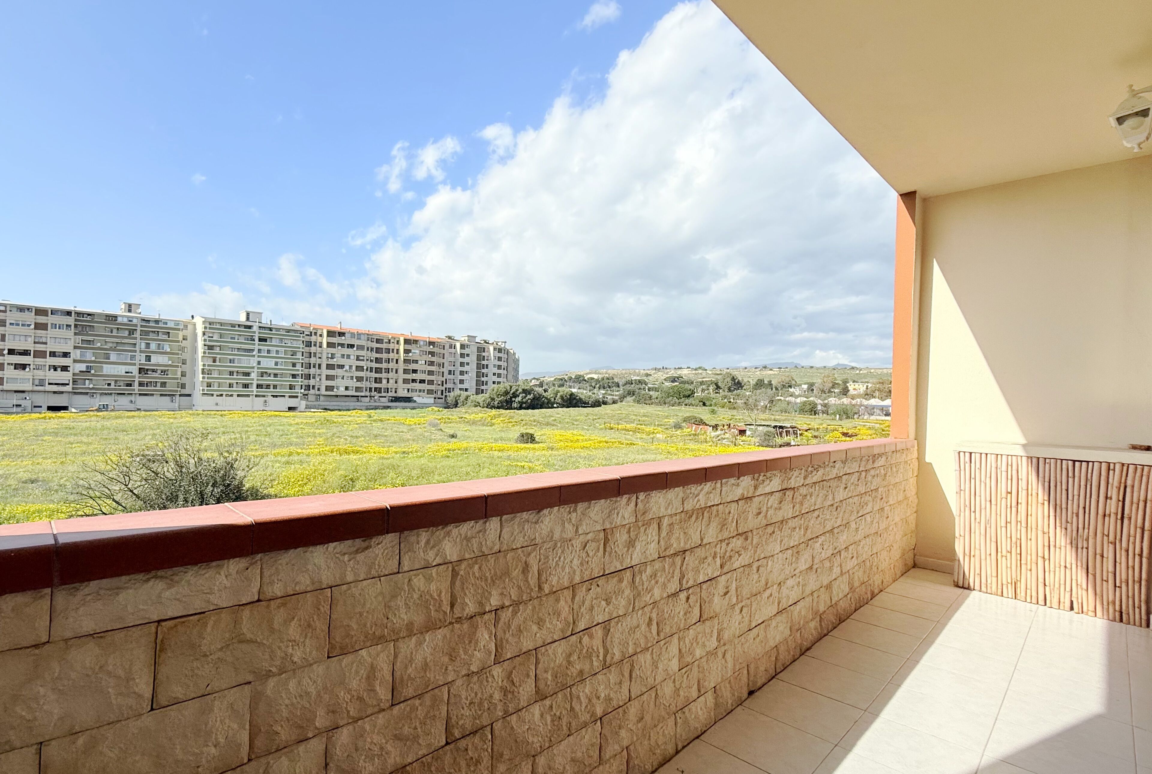 Un balcón con pared de piedra y vistas a un edificio grande y un área ajardinada.