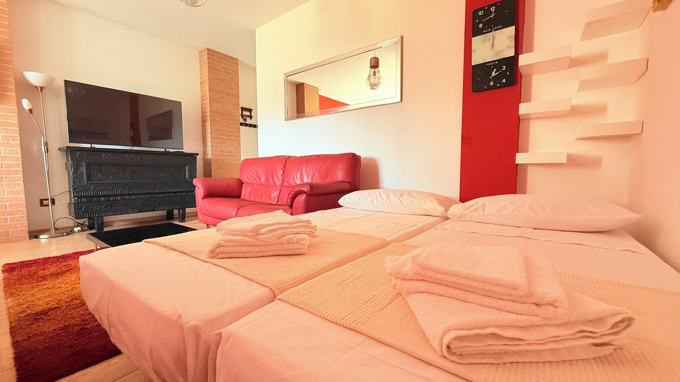 Une chambre d’hôtel avec un lit, un fauteuil rouge, un téléviseur à écran plat, une cheminée et une horloge murale.