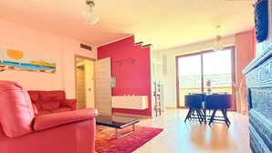 A modern living room with a red sofa, a glass coffee table, and a dining area with a white table and blue chairs. - Spacious 2BR Apartment for 6 • Parking • 20 min Walk to Beach (Quartu Sant'Elena)