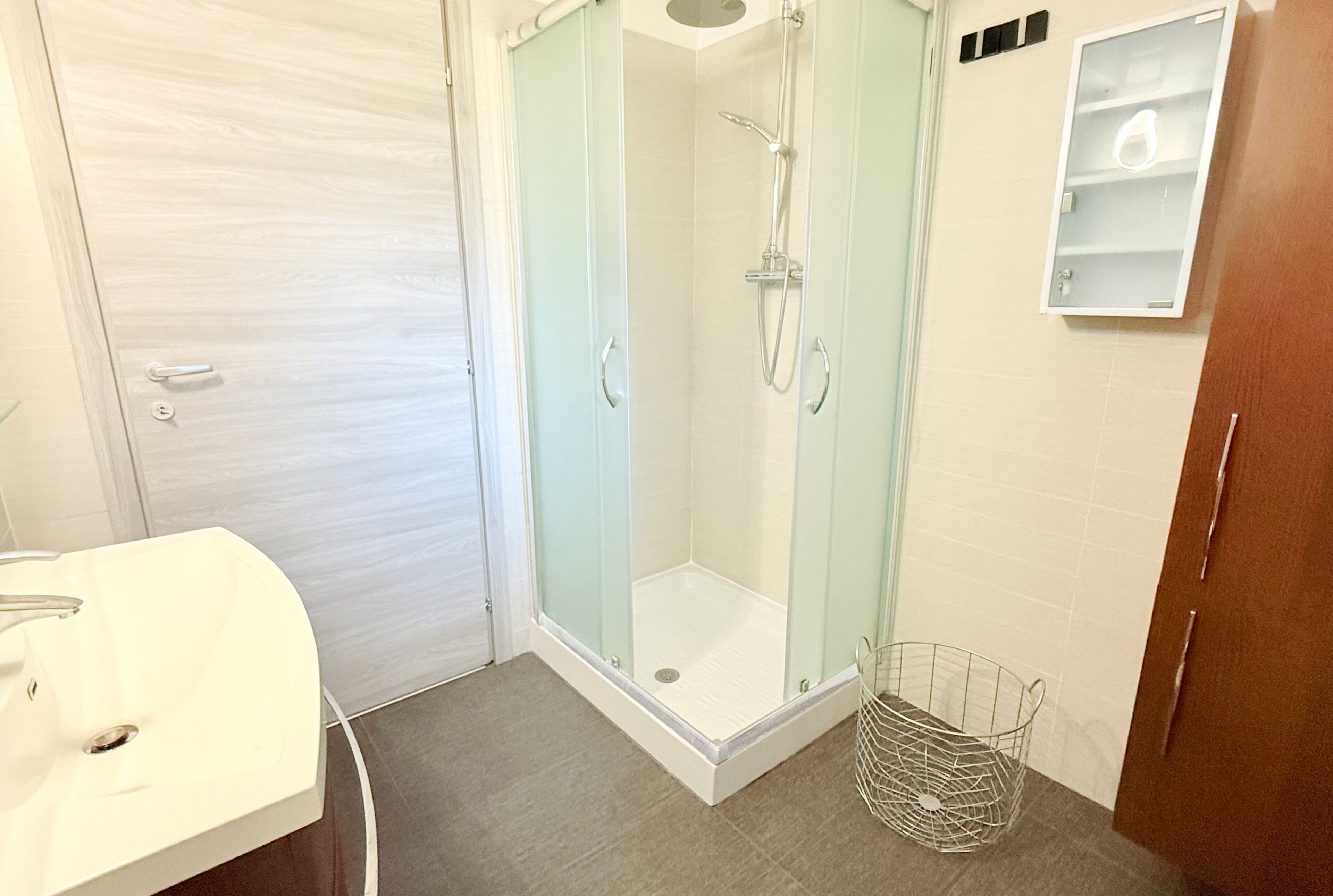 Ein Badezimmer mit einer Glaskabine zur Dusche, einem weißen Waschbecken und einem kleinen Schrank.