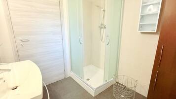 Ein Badezimmer mit einer Glaskabine zur Dusche, einem weißen Waschbecken und einem kleinen Schrank.