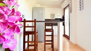 A modern kitchen with white cabinets, a refrigerator, and a wooden dining table with two chairs. - Spacious 2BR Apartment for 6 • Parking • 20 min Walk to Beach (Quartu Sant'Elena)