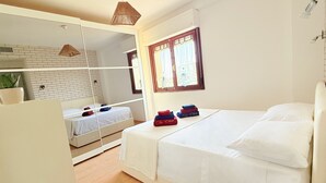 A bedroom with a large bed, a smaller bed, a mirror, and a window with curtains. - Spacious 2BR Apartment for 6 • Parking • 20 min Walk to Beach (Quartu Sant'Elena)