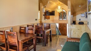 A wooden dining area with a table and chairs, a staircase leading to an upper level, and a television mounted on the wall. - Dogri Homes (Shimla)